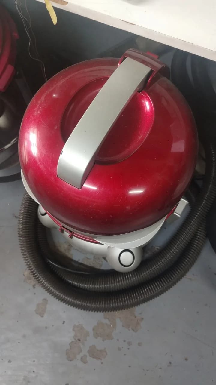 Used red canister vacuum cleaner with visible scratches on the lid
