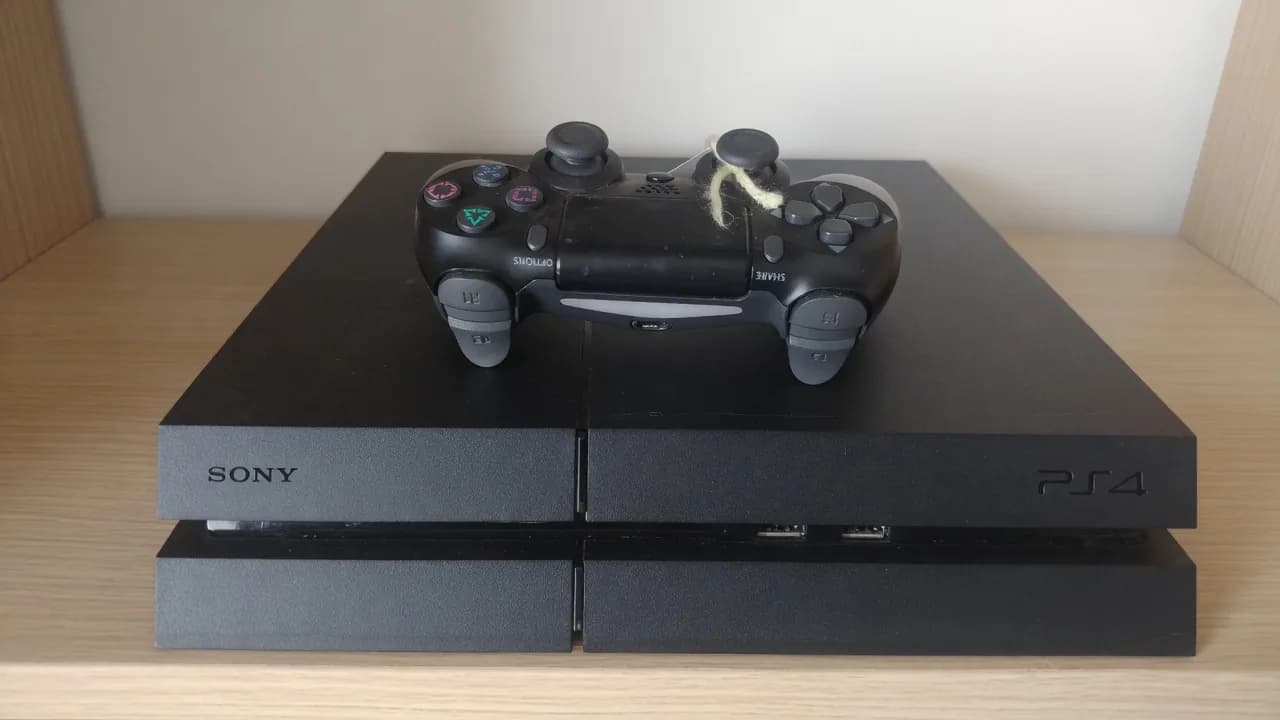 Used black PlayStation 4 with a worn controller on top