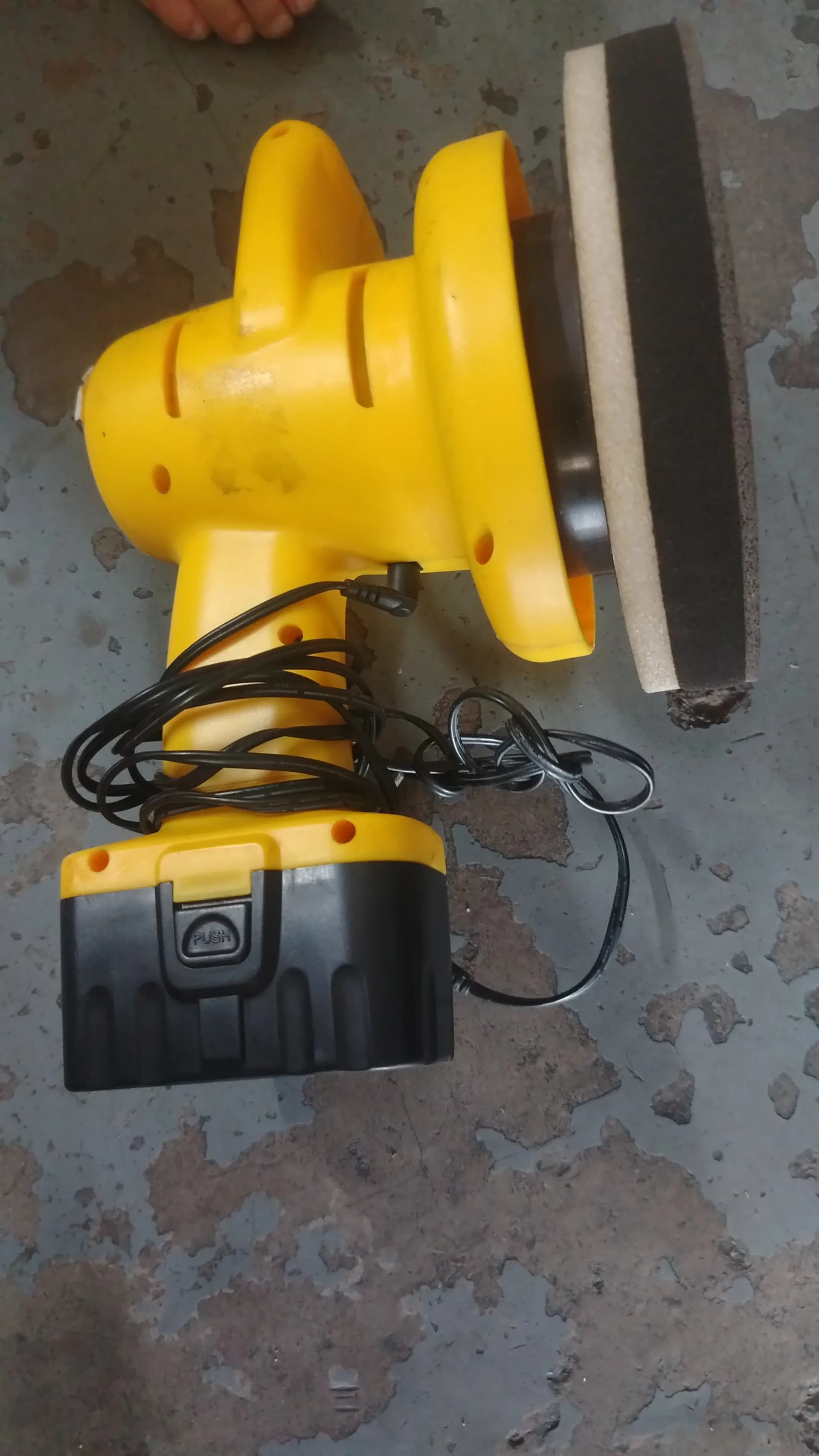 Used yellow cordless polisher with a pad and battery on a concrete floor