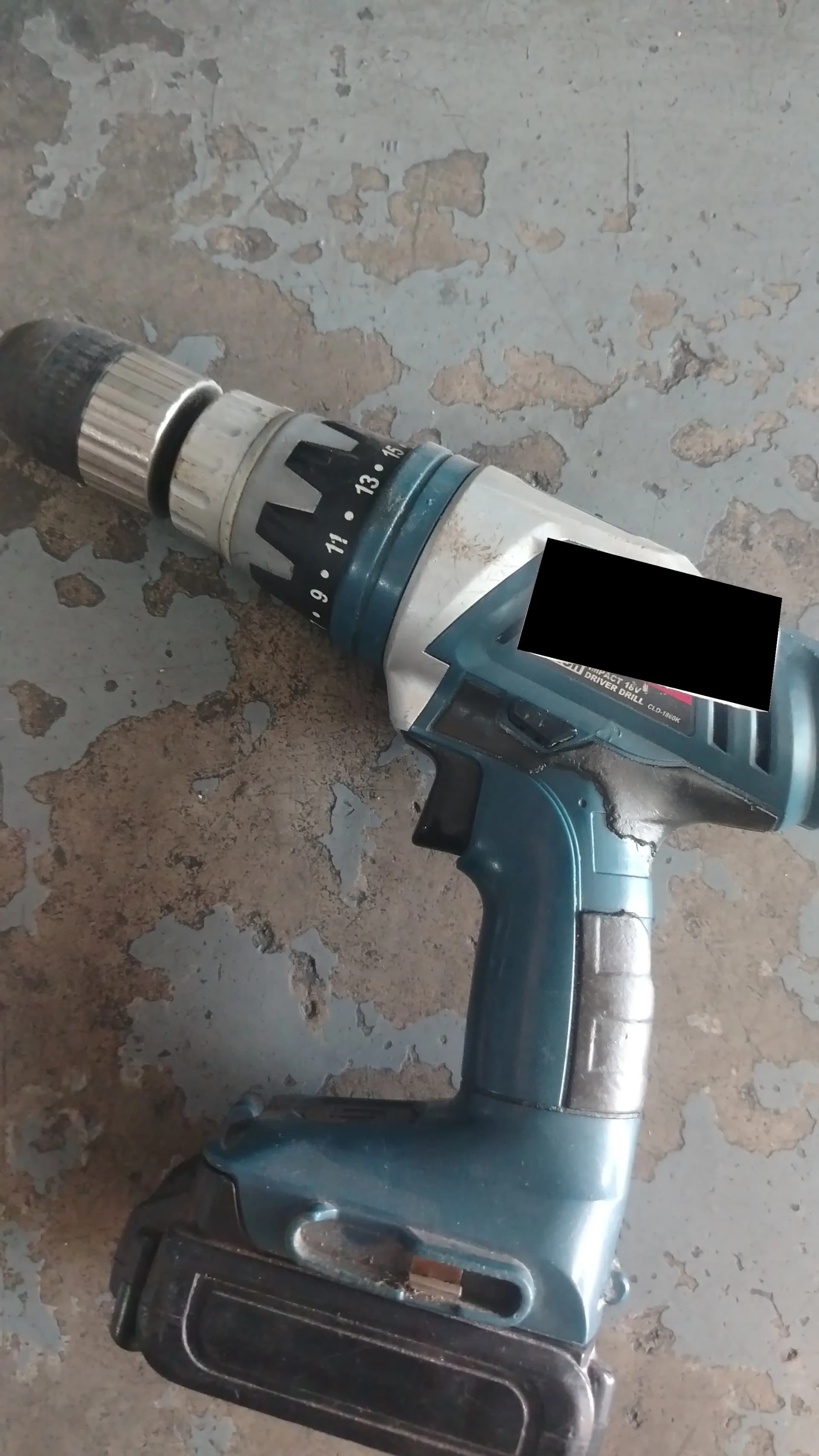 Used teal Ryobi cordless drill with scuffs and a cracked housing