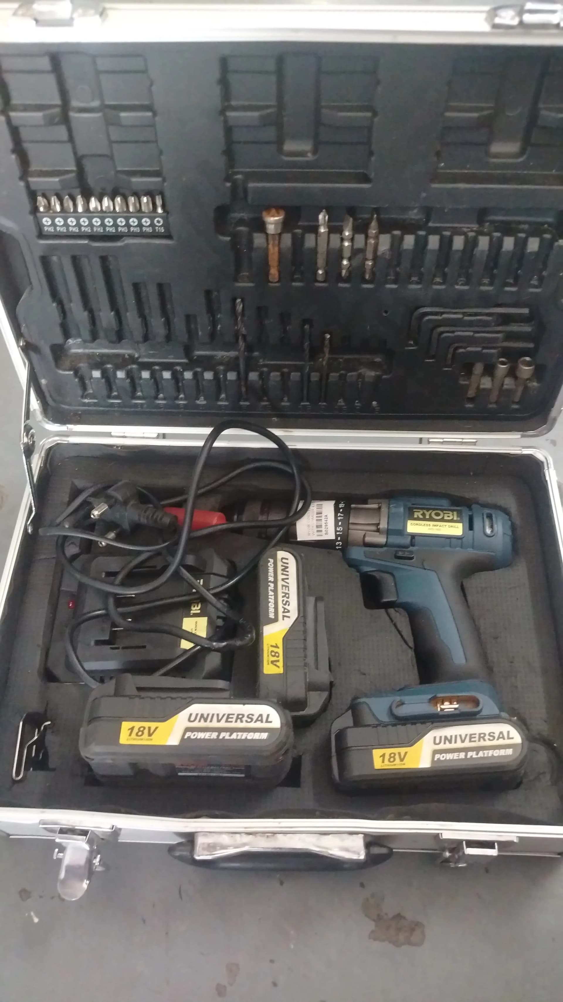 Open case with a used Ryobi 18V impact drill, three batteries, charger and bits